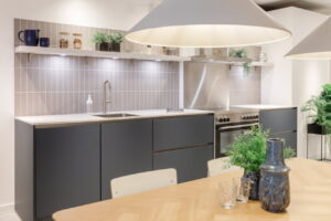 Blauwe moderne woonkeuken met grijze tegelachterwand en inductiefornuis + licht houten eettafel